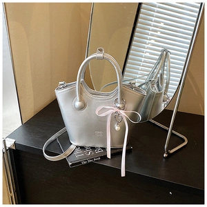 Détail du sac seau argenté avec ruban rose, breloque en cœur et perles élégantes