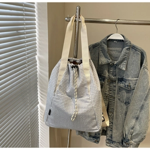 Detail of light blue checkered drawstring bucket bag with cream woven handles