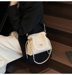 Detail of cream bucket bag with metal chain strap and drawstring on wooden stairs