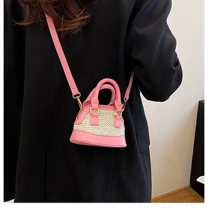 Detailansicht einer kleinen rosa Leder-Muscheltasche mit Strohgeflecht auf schwarzem Mantel