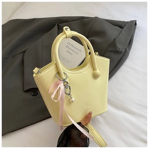 Détail d'un sac seau beige avec breloques cœur et perles sur fond de costume foncé