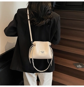 Detail of off-white PU leather bucket bag with brand tag and silver chain on model