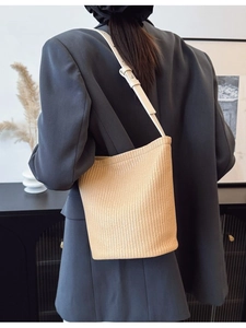 Straw bucket bag with beige leather strap worn over shoulder on a grey blazer