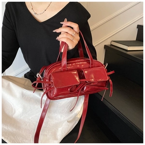 Détail d'un sac bowling rouge brillant en cuir verni avec des nœuds et des poches avant