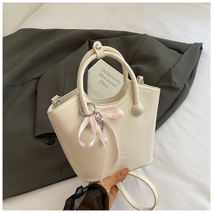 Détail d'un sac seau en cuir blanc crème avec un ruban rose et une bandoulière amovible