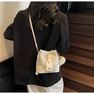 Detail of a white bucket bag with geometric prints and a plush bear charm worn by a model