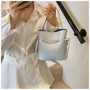 Close-up of light gray bucket bag showing polished leather texture and drawstring detail