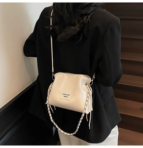 Detail of off-white bucket bag featuring woven chain strap and pleated leather design