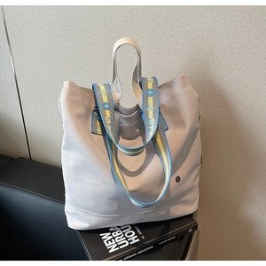 Detail of light grey nylon tote with jacquard strap and round metal logo on books