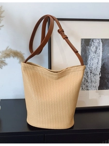 Minimalist beige woven bucket bag with adjustable brown shoulder strap in a cozy interior setting