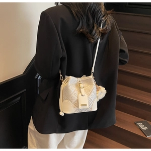 Detail of cream bucket bag featuring geometric patterns and plush ball charm on a model