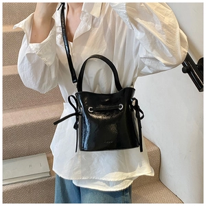 Detail view of a black glossy bucket bag with drawstring and thin shoulder strap