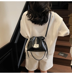 Detail of black leather bucket bag with drawstring closure and metal chain strap