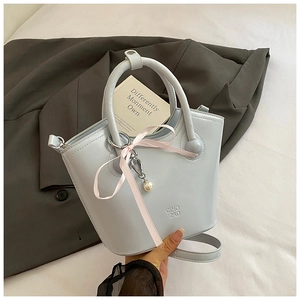 Détail du sac seau en cuir bleu clair avec ruban rose et pendentif en perle blanche