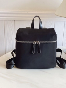 Minimalist black nylon backpack with silver dual zippers on a marble tabletop