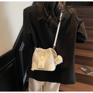 Detail view of white monogram bucket bag with pompom charm on a stylish model