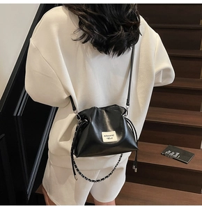 Detail of black drawstring bucket bag with metal chain strap worn by casual model