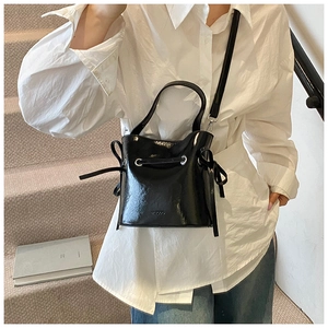 Detail of a black glossy patent leather bucket bag with silver hardware and drawstrings