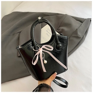 Détail d'un sac seau noir en cuir avec un nœud en soie rose et un pendentif perle