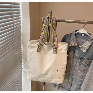 Detail of white canvas tote bag featuring contrast woven straps and metal logo badge