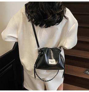 Detail of black glossy drawstring bucket bag with metal chain strap worn by a model