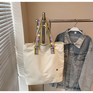 Detail of white canvas tote bag featuring a colorful woven shoulder strap and metal logo