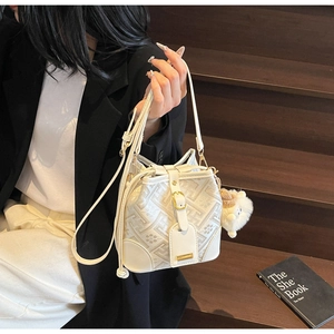 Detail view of cream bucket bag with geometric patterns, gold hardware and plush charm