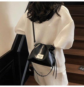 Detail of black drawstring bucket bag with leather chain strap on wooden stairs