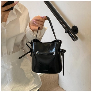 Detail of glossy black patent leather bucket bag with silver eyelets and drawstring