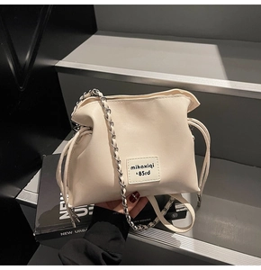 Detail of cream drawstring bucket bag with chain strap and vintage style patch