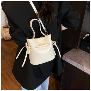 Chic cream bucket bag with decorative side bow and slim strap worn by a model