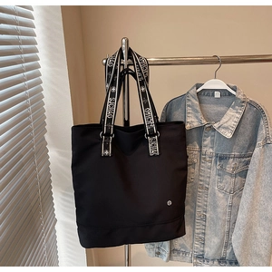 Detail view of black canvas tote bag with lettered webbing handles and metal logo