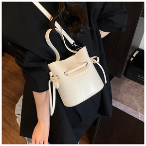 Detail of a creamy white drawstring bucket bag shown worn as a crossbody on a dark model