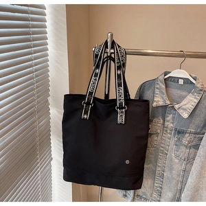Close-up of black tote bag with SJCHAO lettered webbing straps and metal logo detail