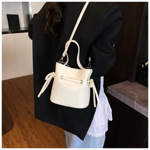 Detail of a creamy white bucket bag with pebble leather texture and embossed logo