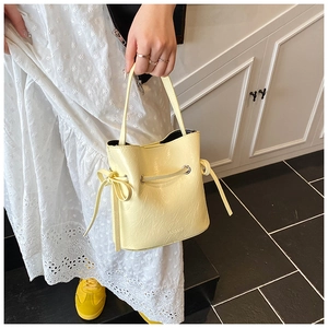 Detail of a creamy yellow drawstring bucket bag with pleated texture and bow decoration