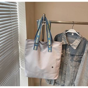 Close-up of a grey canvas tote bag with blue and yellow contrasting straps on a hanger