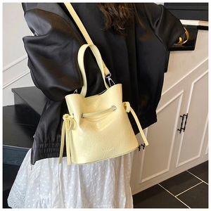 Detail of light yellow bucket bag with drawstring closure and embossed MUDUO logo on leather