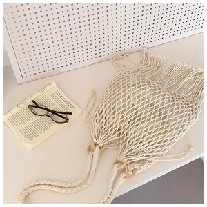 Détail d'un sac en filet beige tissé main avec franges et poignée en bois ronde
