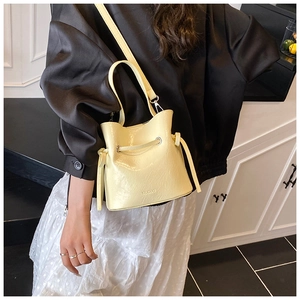 Detail of a creamy yellow drawstring bucket bag with glossy texture and MUDUO branding