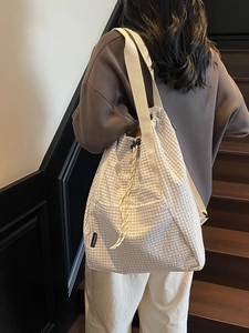 Plaid canvas drawstring tote bag with wide shoulder strap shown on a model in a modern interior