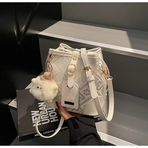 Detail of white bucket bag with geometric patterns, gold buckle and plush sheep charm