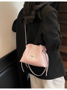 Light pink drawstring bucket bag in glossy faux leather with elegant chain strap