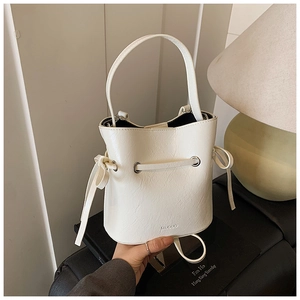 Detailed macro view of white leather bucket bag with bow drawstring and brand lettering