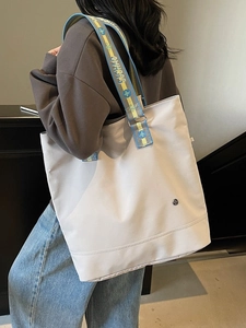 Large beige canvas tote bag with contrast woven strap worn by model for daily commute