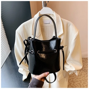 Detail of glossy black bucket bag featuring drawstring closure and metallic hardware
