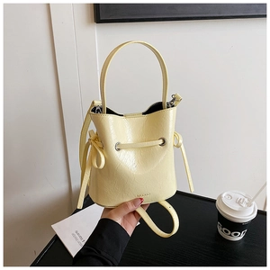 Close-up of pale yellow wrinkled texture bucket bag with a decorative bow and handle