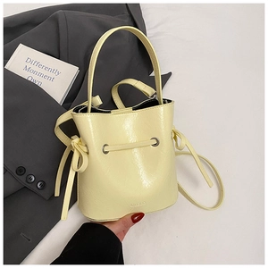 Detail of a creamy yellow drawstring bucket bag with shiny wrinkled texture and brand embossing