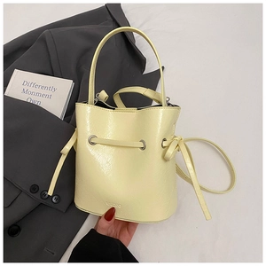 Detail of a creamy yellow drawstring bucket bag with glossy leather and brand logo