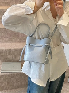 Minimalist light blue drawstring bucket bag shown with top handle and crossbody strap